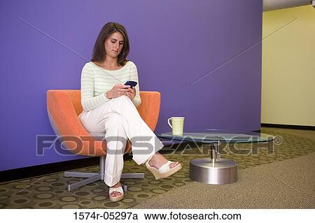 Businesswoman sitting in a chair holding a hand held device View Large Photo Image Stock Image - Businesswoman sitting in a chair holding a hand held device. Fotosearch