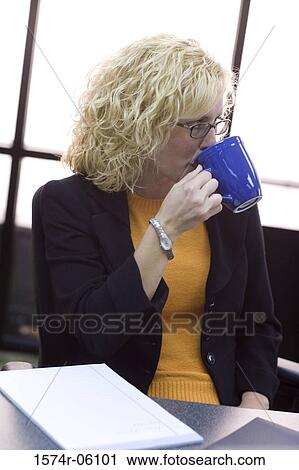 Stock Image - Businesswoman sitting in an office drinking coffee. Fotosearch