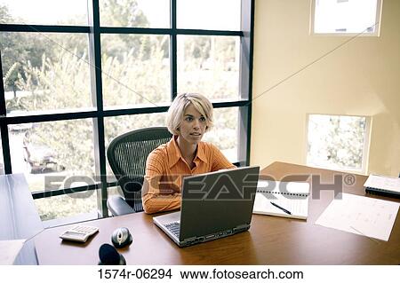 Businesswoman sitting in front of a laptop in an office View Large Photo Image Picture - Businesswoman sitting in front of a laptop in an office. Fotosearch
