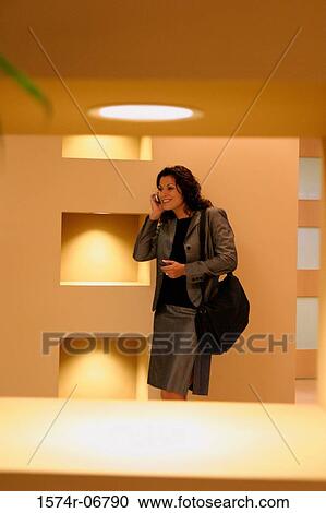 Stock Image - Businesswoman standing in a corridor using a mobile phone. Fotosearch