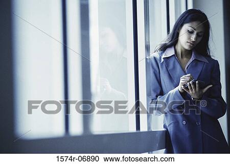 Stock Image - Businesswoman standing operating a hand held device. Fotosearch