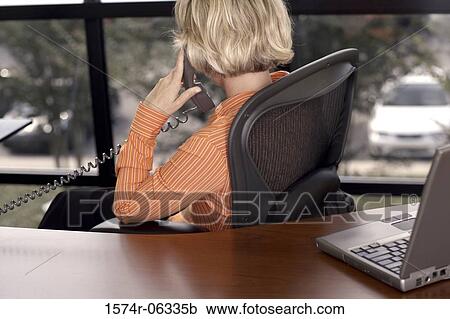 Stock Image - Businesswoman talking on a telephone in an office. Fotosearch