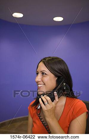 Stock Image - Businesswoman talking on a telephone in an office. Fotosearch