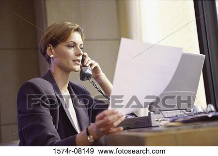 Stock Photo - Businesswoman talking on a telephone while reading a document. Fotosearch