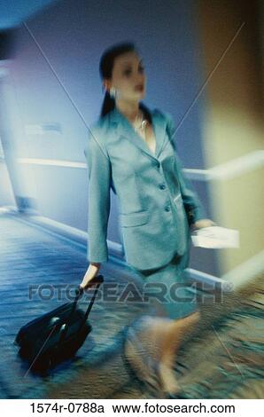 Stock Image - Businesswoman walking in a corridor with a suitcase. Fotosearch