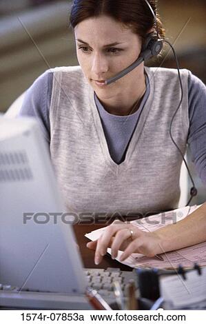 Stock Image - Businesswoman wearing a headset working on a computer. Fotosearch