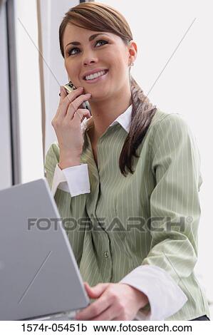 Close-up of a businesswoman holding a laptop using a mobile phone View Large Photo Image Stock Image - Close-up of a businesswoman holding a laptop using a mobile phone. Fotosearch