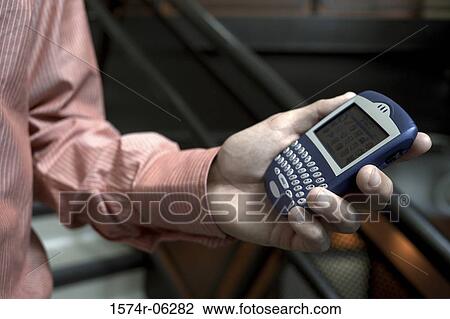 Stock Image - Close-up of a person's hand holding a hand held device. Fotosearch