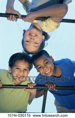 Stock Image - Close-up of two boys and a girl playing on monkey bars. Fotosearch