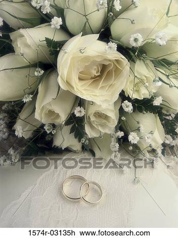 Stock Image - Close-up of wedding rings with a bouquet of flowers. Fotosearch