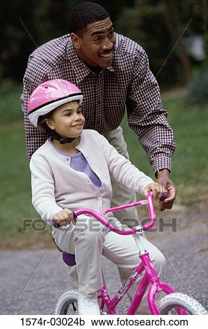 Stock Image - Father teaching his daughter cycling. Fotosearch