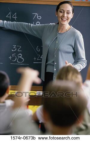 Female teacher pointing to a chalkboard in a classroom View Large Photo Image Stock Image - Female teacher pointing to a chalkboard in a classroom. Fotosearch