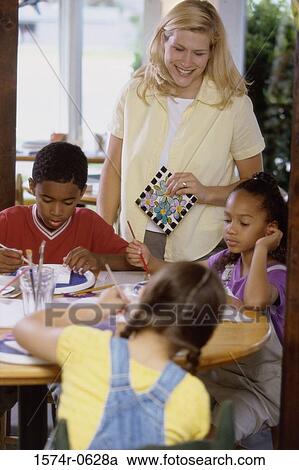 Stock Image - Female teacher watching her students coloring. Fotosearch