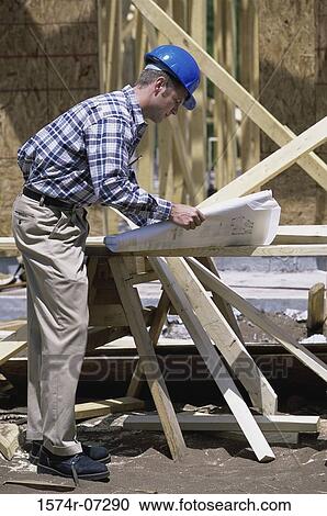 Stock Image - Foreman standing at a construction site holding blueprints. Fotosearch