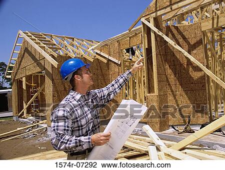 Stock Image - Foreman standing at a construction site holding blueprints. Fotosearch