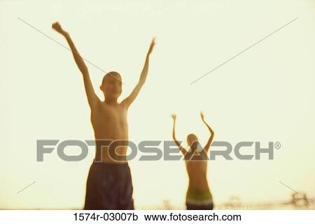 Stock Image - Front view of two boys standing with their arms raised. Fotosearch