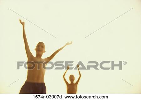 Stock Image - Front view of two boys standing with their arms raised. Fotosearch