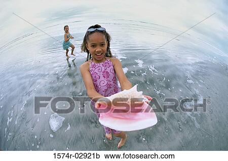 Girl standing on the beach holding a conch shell View Large Photo Image Stock Image - Girl standing on the beach holding a conch shell. Fotosearch