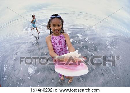 Girl standing on the beach holding a conch shell View Large Photo Image Stock Image - Girl standing on the beach holding a conch shell. Fotosearch