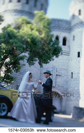 Stock Image - Groom helping his bride into an antique car. Fotosearch
