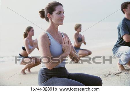 Stock Image - Group of people meditating on the beach. Fotosearch