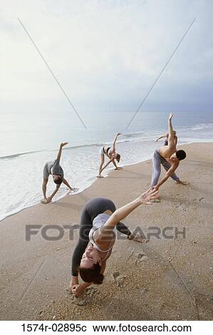 Stock Image - Group of people performing yoga on the beach. Fotosearch