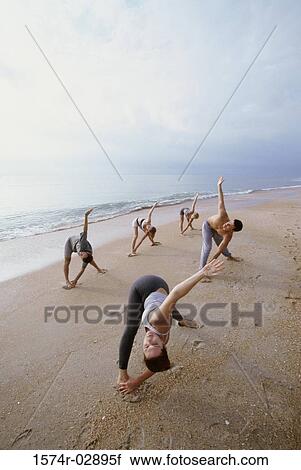 Stock Image - Group of people performing yoga on the beach. Fotosearch