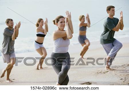 Stock Image - Group of people performing yoga on the beach. Fotosearch