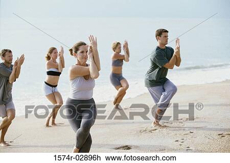 Stock Image - Group of people performing yoga on the beach. Fotosearch