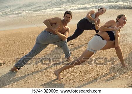 Stock Image - Group of people performing yoga on the beach. Fotosearch