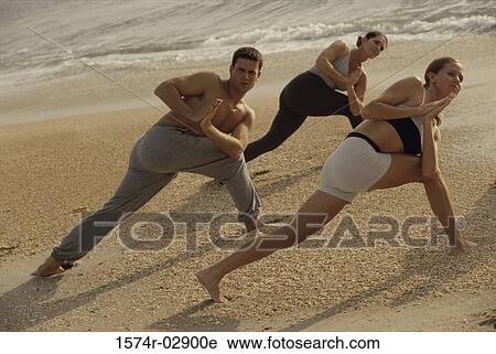 Stock Image - Group of people performing yoga on the beach. Fotosearch