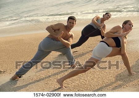 Stock Image - Group of people performing yoga on the beach. Fotosearch