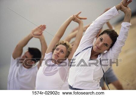 Stock Image - Group of people performing yoga on the beach. Fotosearch