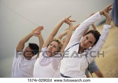 Stock Image - Group of people performing yoga on the beach. Fotosearch