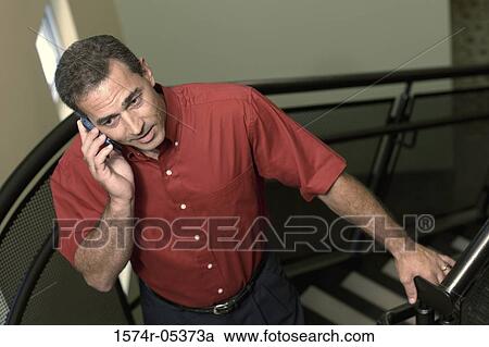 Stock Image - High angle view of a businessman standing on a staircase talking on a mobile phone. Fotosearch
