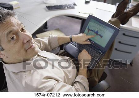 High angle view of a businessman working on a laptop looking at camera View Large Photo Image Stock Image - High angle view of a businessman working on a laptop looking at camera. Fotosearch