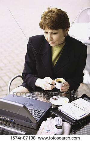Stock Photo - High angle view of a businesswoman holding a cup of coffee looking at a laptop. Fotosearch