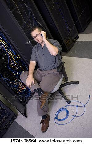 Picture - High angle view of a technician talking on a mobile phone in a server room. Fotosearch