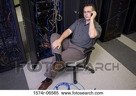 Stock Photography - High angle view of a technician using a mobile phone in a server room. Fotosearch