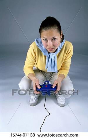 High angle view of a young woman squatting and holding a game joystick View Large Photo Image Stock Photo - High angle view of a young woman squatting and holding a game joystick. Fotosearch