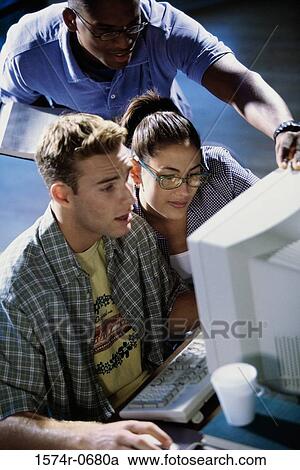 Stock Image - High angle view of two young men and a young woman using a computer. Fotosearch