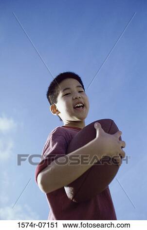 Stock Image - Low angle view of a boy holding a football. Fotosearch