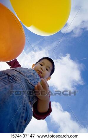 Low angle view of a boy holding balloons View Large Photo Image Stock Photo - Low angle view of a boy holding balloons. Fotosearch