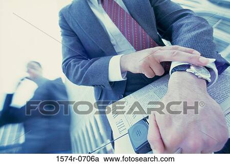Stock Image - Low angle view of a businessman looking at his wristwatch. Fotosearch