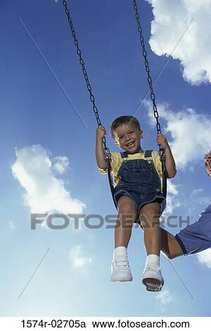 Stock Image - Low angle view of a father pushing his son on a swing. Fotosearch