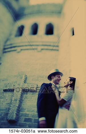 Stock Image - Low angle view of a newlywed couple embracing each other. Fotosearch