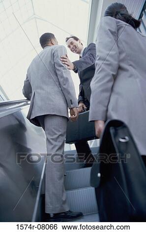 Stock Photograph - Low angle view of two businessmen and a businesswoman on an escalator. Fotosearch