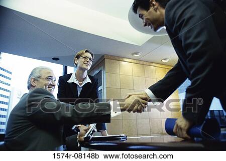 Low angle view of two businessmen shaking hands with a businesswoman standing in the background View Large Photo Image Stock Image - Low angle view of two businessmen shaking hands with a businesswoman standing in the background. Fotosearch