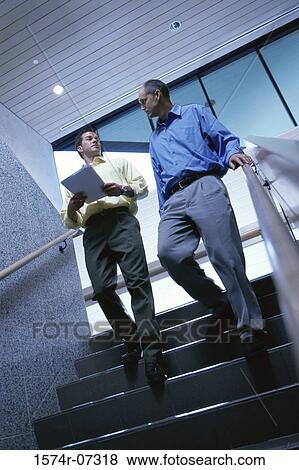 Stock Photo - Low angle view of two businessmen walking down stairs. Fotosearch