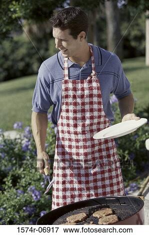 Stock Photo - Man standing with a plate and tongs in front of a barbecue grill. Fotosearch